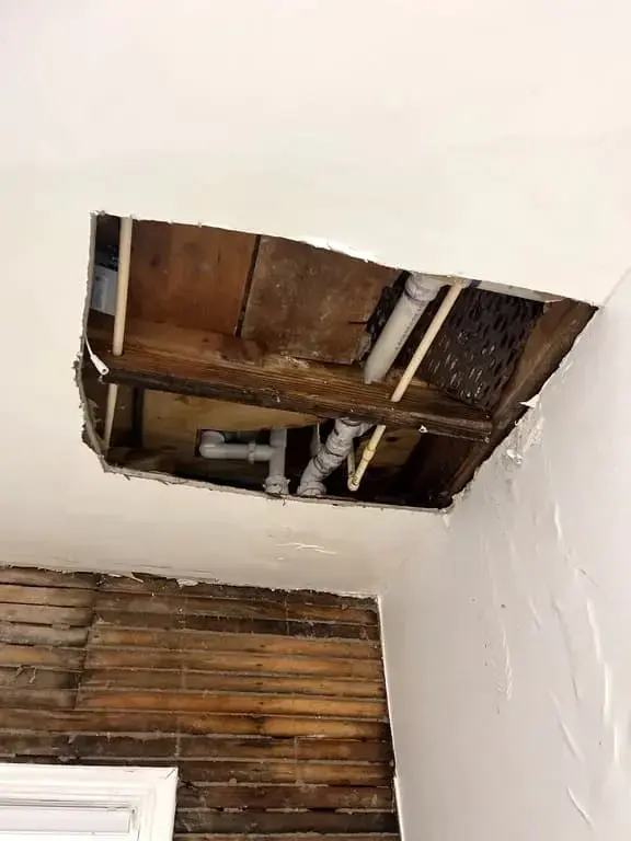 Ceiling opened below a burst pipe, exposing the supply and drain lines
