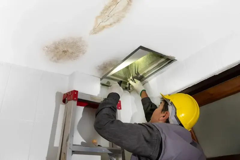 Worker checking the attic hatch under a water-stained ceiling after a roof leak